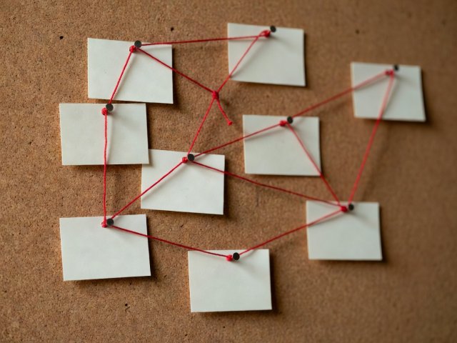 Shallow-focus close-up of index cards pinned to cork board and joined by red thread